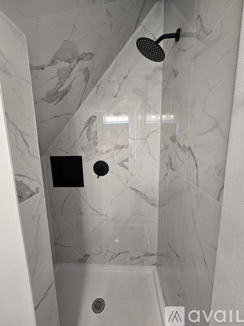 A shower area with a marble wall and a black shower head.