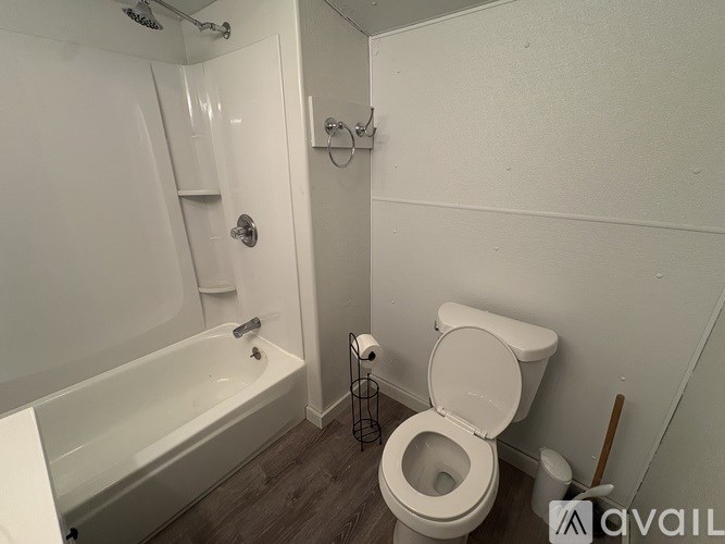A white toilet is in a small bathroom with a white tub and towel rack.