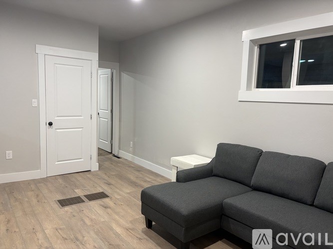 A grey couch sits in a room with a white door and a window.