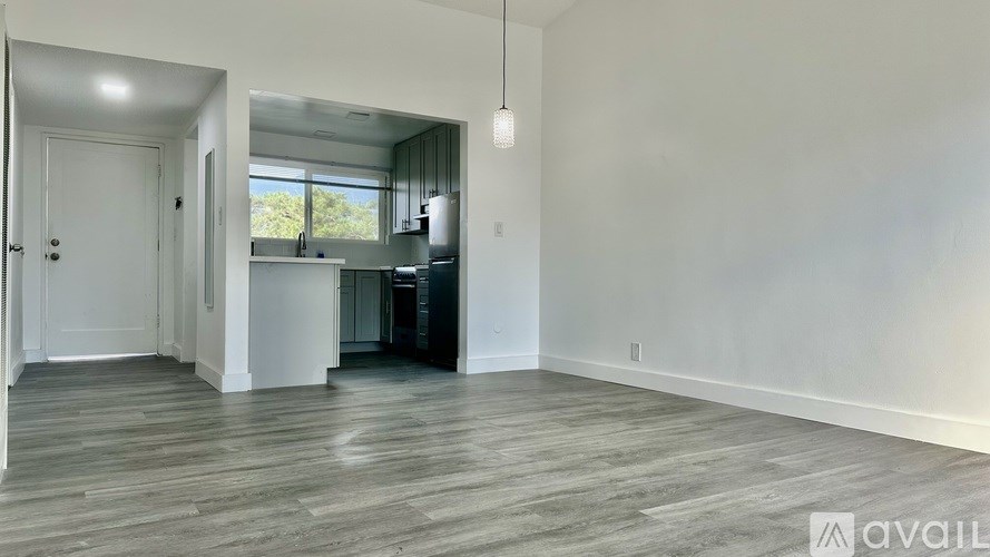 A spacious room with wooden flooring and a kitchen area in the background.