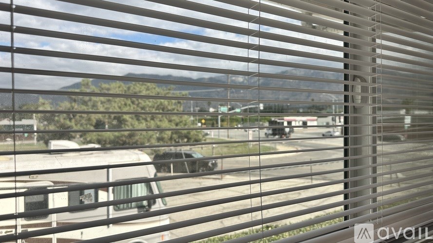 A view through a window with blinds, showing a parking lot and a mountain in the distance.