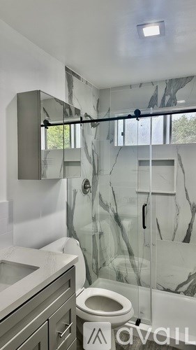 A bathroom with a toilet, sink and a glass shower door.