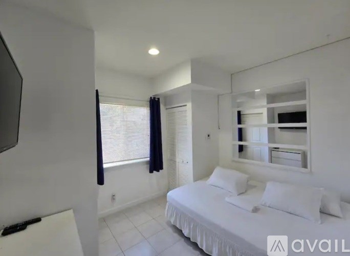 A bedroom with a bed, a window with black curtains, and a mirror on the wall.