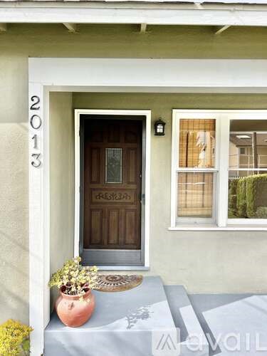 A house numbered 2013 has a brown door and a flower pot on the steps.