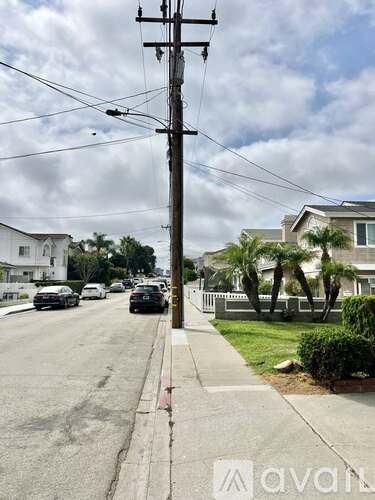 A street view with cars parked on the side and a utility pole in the foreground.