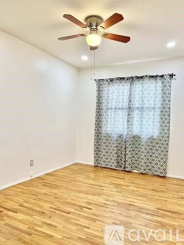 A room with a ceiling fan and a window with curtains.