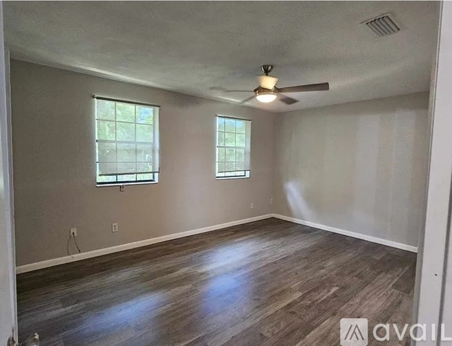 A room with wooden flooring and two windows.