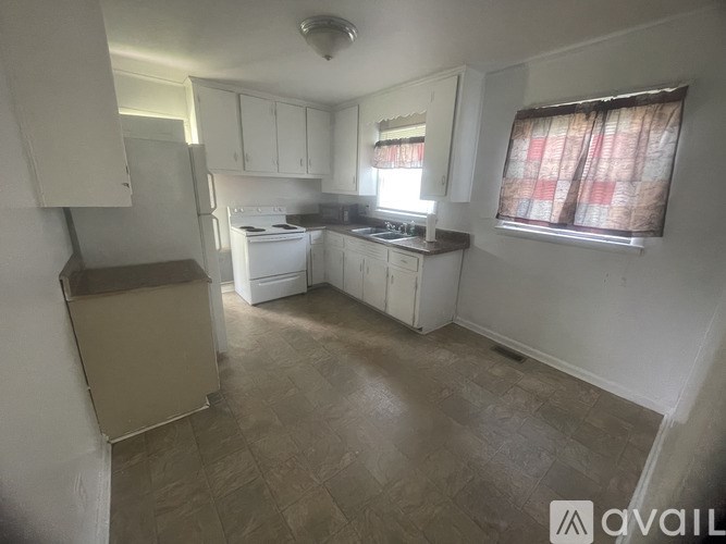 A kitchen with white cabinets and a window with a red curtain.