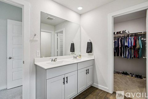 A bathroom with a white sink vanity and a closet with clothes hanging.