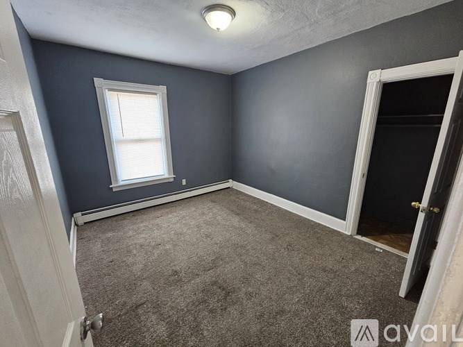 A room with a carpeted floor, a window with blinds, and a door.