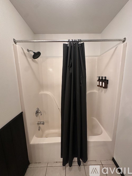 A black shower curtain is hanging in a white bathroom.