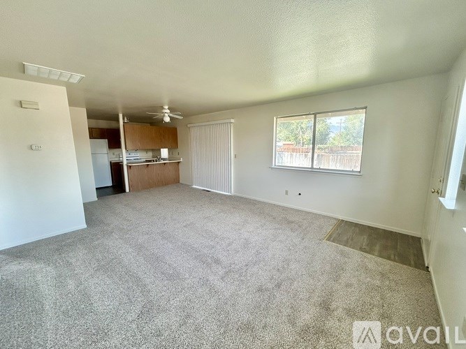 A spacious living room with a carpeted floor and a ceiling fan.