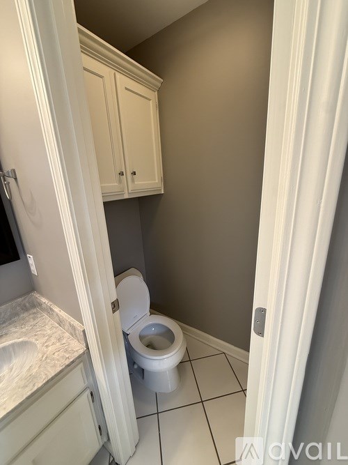 A white toilet in a small bathroom with a white cabinet.