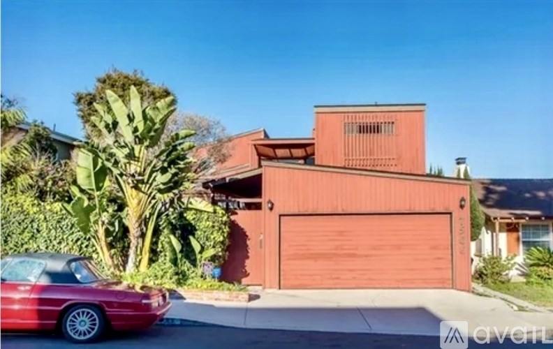 A red car is parked in front of a house with a closed brown garage door.