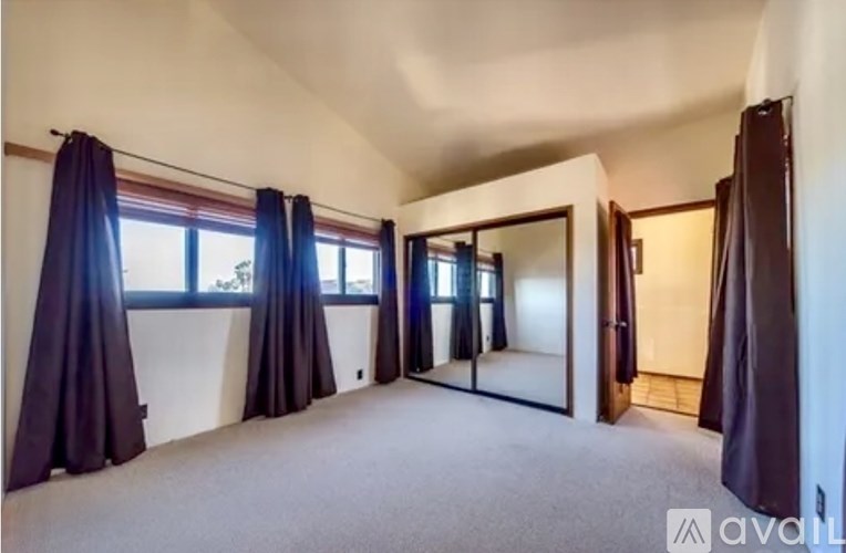 A room with a carpeted floor, a large window with curtains, and a sliding door.