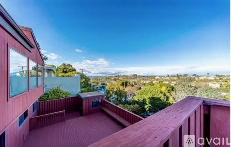 A red building with a balcony overlooking a green landscape.