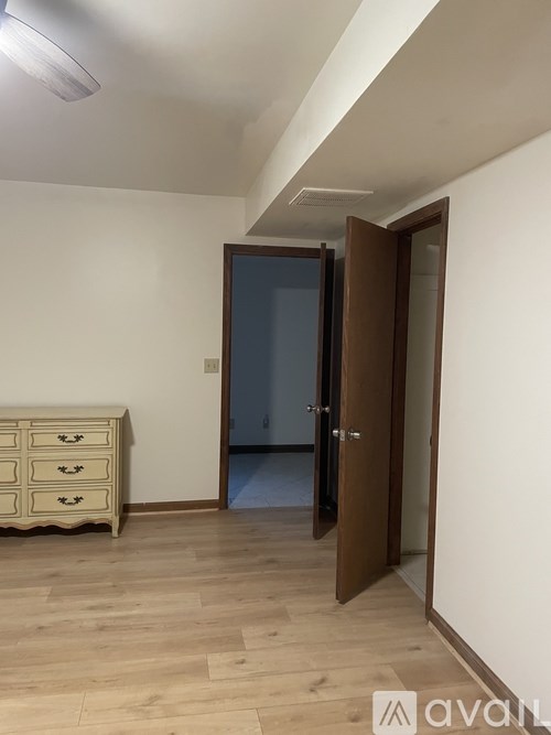 A room with a wooden floor and a white wall with a brown door.