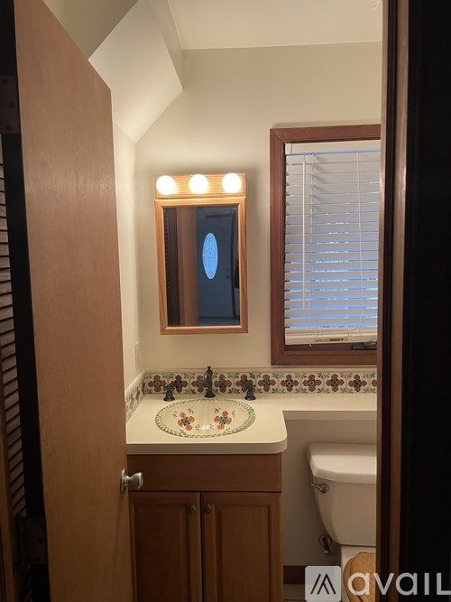 A bathroom with a sink, toilet, and a mirror with lights.