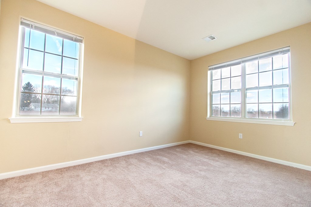 an empty living room with two windows and carpeting