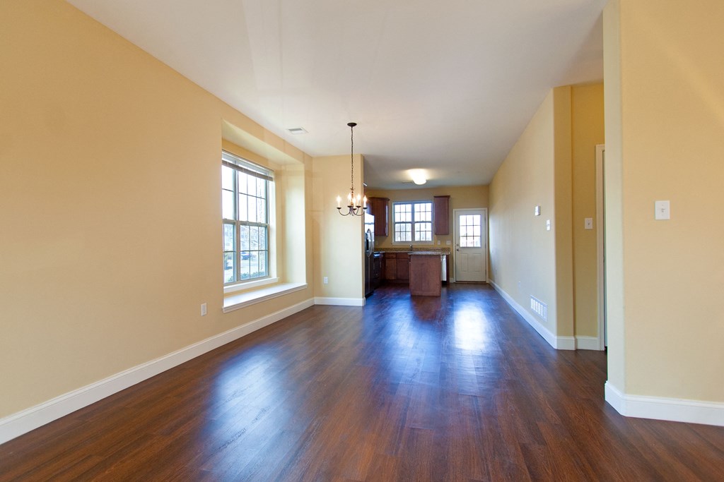 an empty living room with wood floors and a kitchen