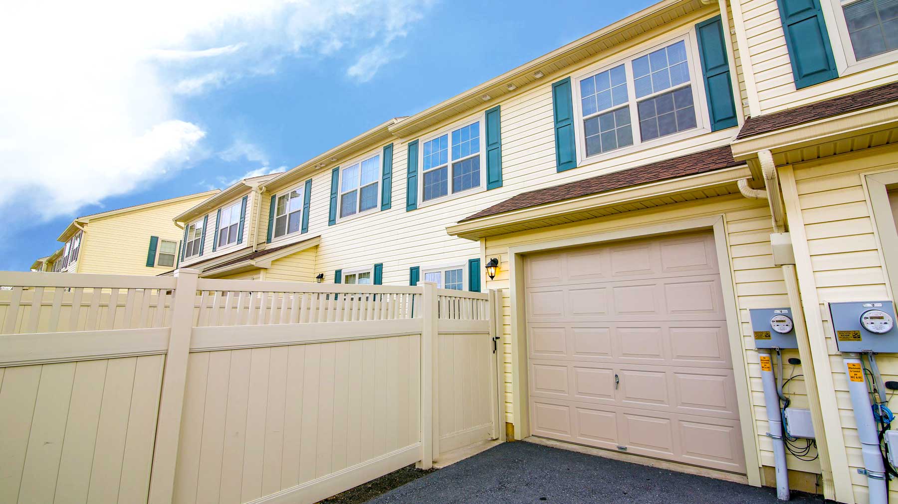 a yellow house with a white fence and two garage doors