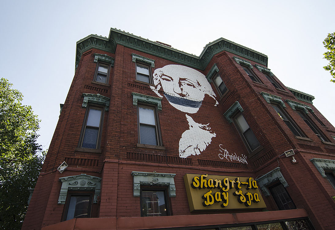 A red building with a large mural of a man's face and the words "Shangri-La Day Spa" written below it.