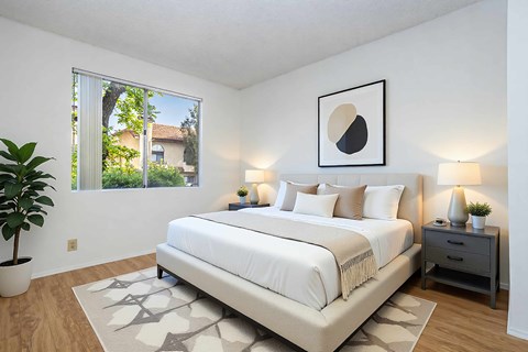 A bedroom with a large bed, a potted plant, and a framed picture on the wall.