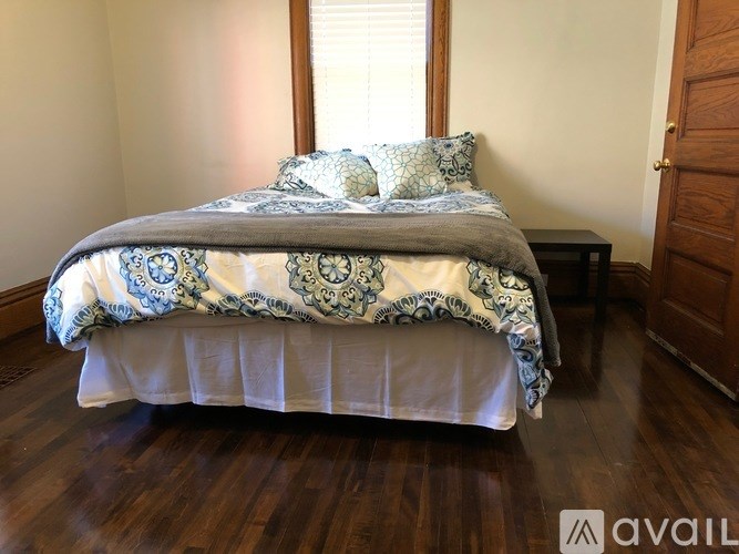 A bed with a blue and white comforter is in a room with wooden floors and a window.