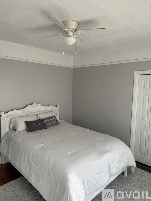 A bedroom with a white bed and a ceiling fan.