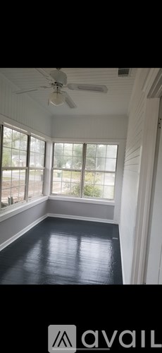 A room with a ceiling fan and large windows.