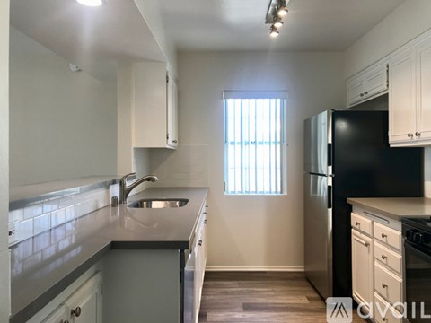 A kitchen with a black refrigerator and a window with blinds.
