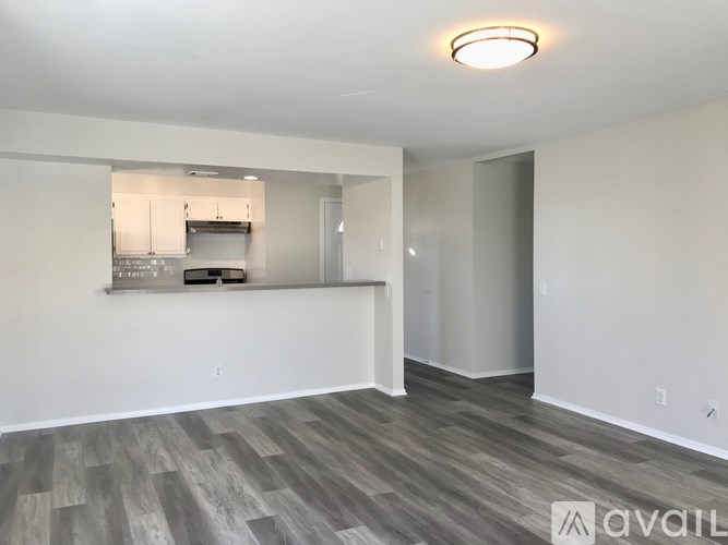 A spacious room with a kitchen area in the background and a wooden floor.