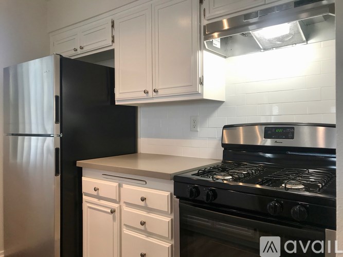 A kitchen with a black refrigerator, white cabinets, and a stainless steel stove.