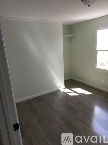 A room with wooden flooring and a window letting in sunlight.