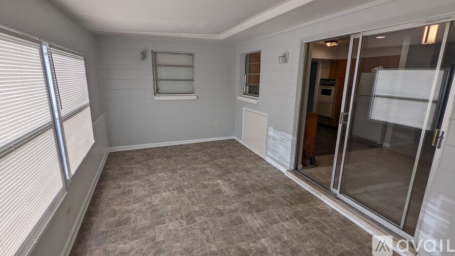 A room with a carpeted floor, a window with blinds, a door with a glass panel, and a small window with a wooden frame.
