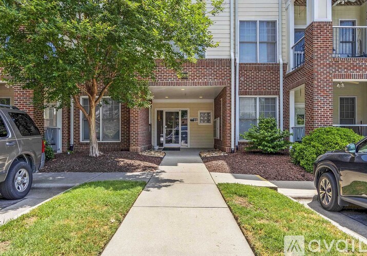 A brick apartment building with a tree in front and cars parked on the street.
