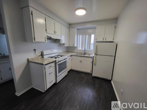A kitchen with white cabinets and appliances, a window, and a wooden floor.