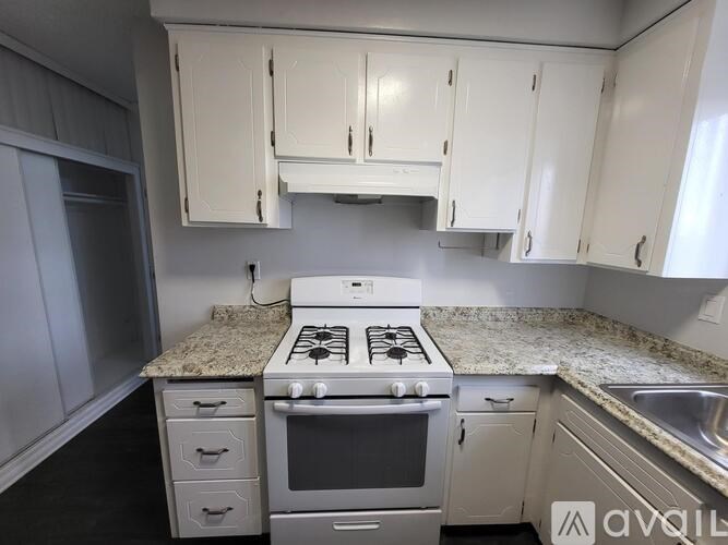 A kitchen with a white stove top oven and white cabinets.