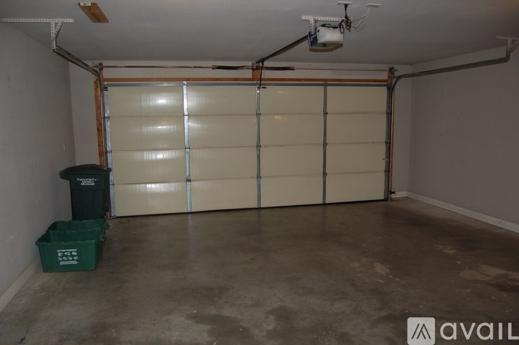 A room with a white wall, a white ceiling, a white garage door, and a green trash can.