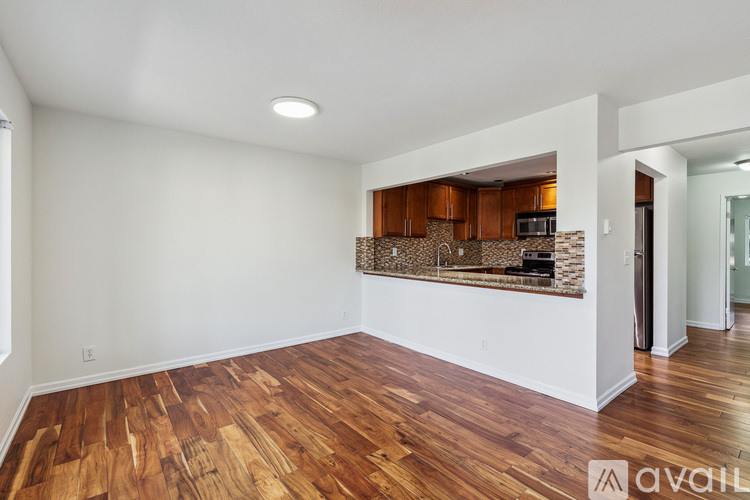 A spacious room with wooden flooring and a kitchen area in the background.