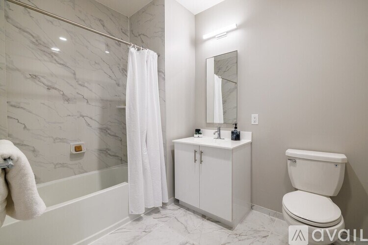 A white bathroom with a marble wall and a white towel hanging on the tub.