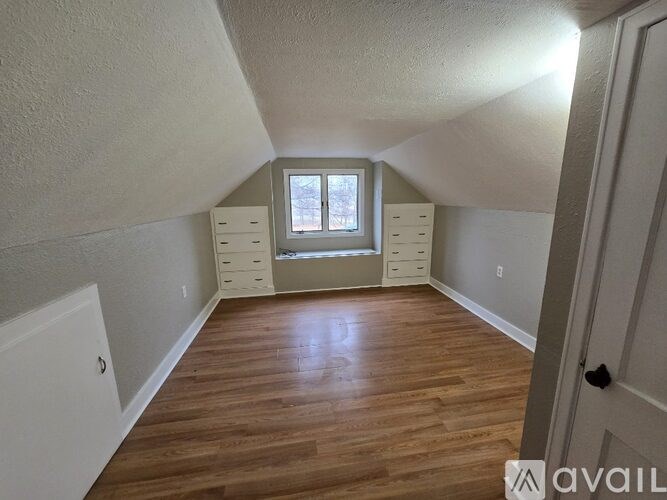 A room with wooden floors and white walls, with a window and drawers.