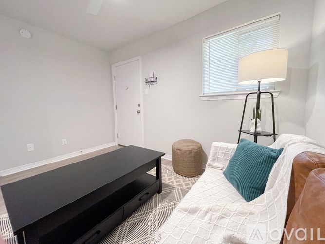 A living room with a black coffee table, a brown leather couch, and a white rug.