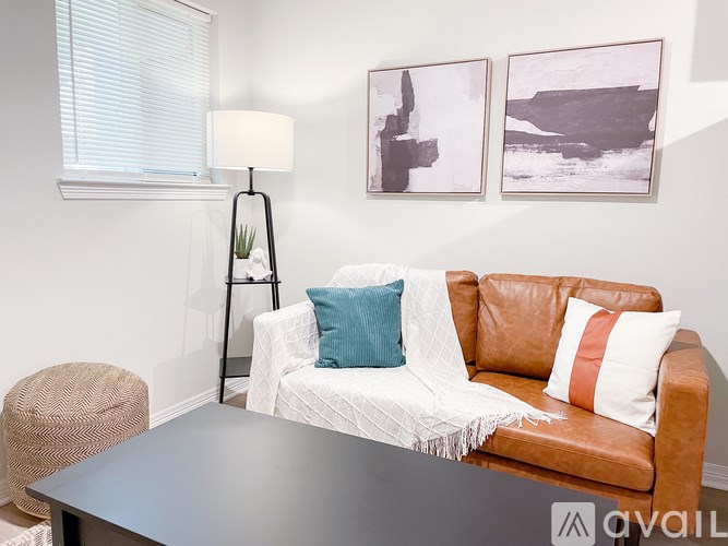 A living room with a brown leather couch, a white throw blanket, a black floor lamp, and two framed pictures on the wall.