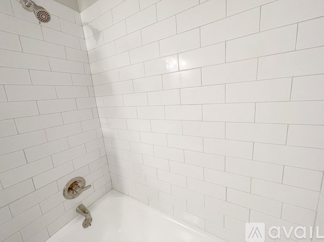A white tiled shower with a shower head and faucet.
