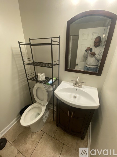 A man is taking a picture of a bathroom with a toilet, sink, and mirror.