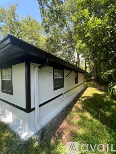 A white and black mobile home sits in a grassy area with trees in the background.