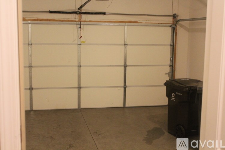 A black trash can sits in front of a white garage door.