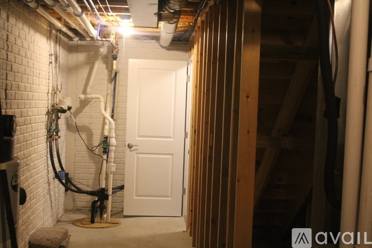 A white door is in a room with a brick wall and pipes.