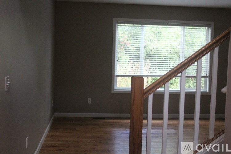 A room with a wooden staircase leading to a window with blinds.